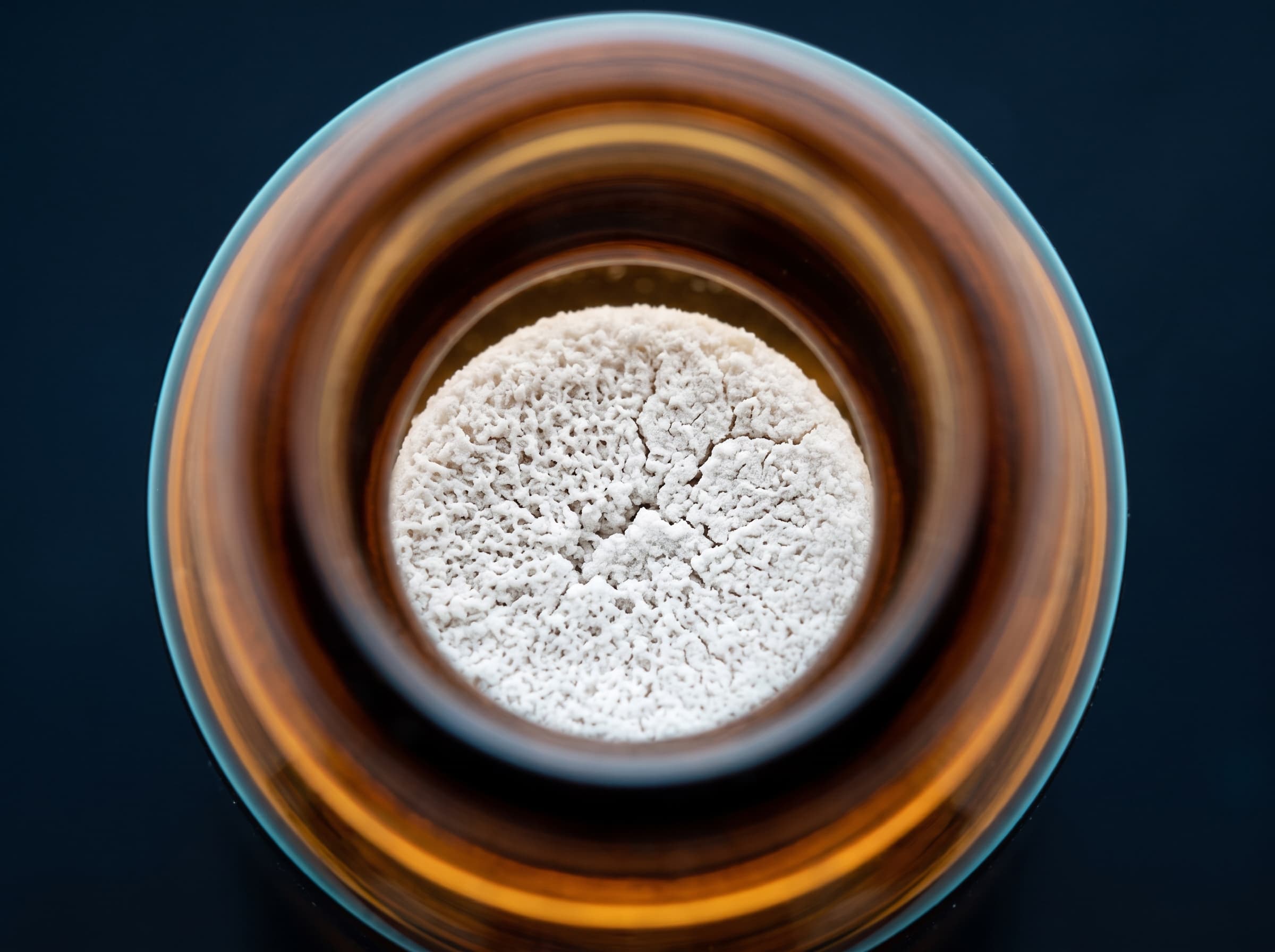 Lyophilized peptide cake inside an amber glass vial, viewed from above.